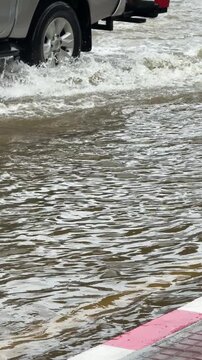Vertical 4K close up video showing floodwater reaching one third of car tire height as vehicles wade through flooded road.