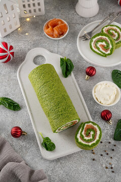 Festive spinach roll with cream cheese and smoked salmon filling on a serving board on a gray background. Christmas holiday appetizer. Top view, copy space.