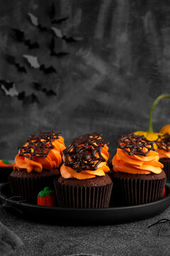 Halloween chocolate cupcakes with orange frosting and chocolate spider web on a dark background. Festive dessert. Funny food idea. Copy space.