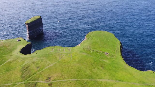 Aerial view of Dun Briste Sea Stack and dramatic coastal cliffs with lush green grass and the Eire sign visible near the edge in Ballycastle, County Mayo, Ireland.