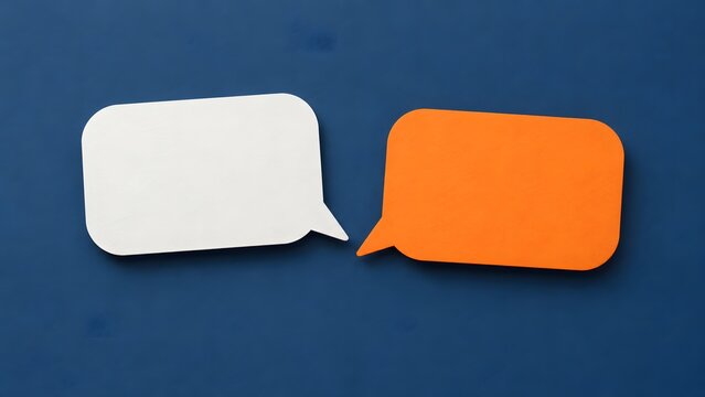 White and orange paper speech bubbles facing each other on textured dark blue background, symbolizing conversation, dialogue and communication with copy space