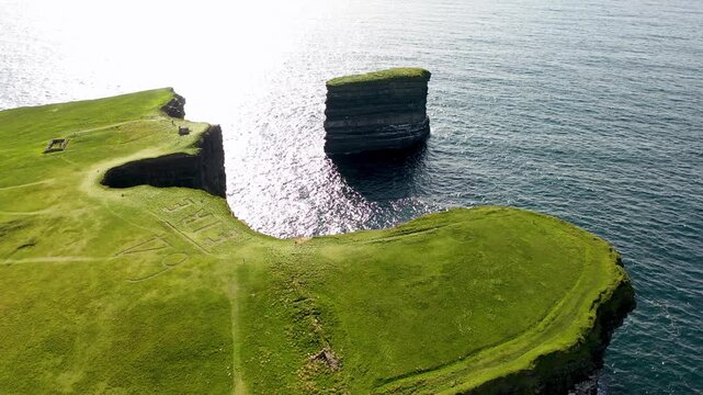 Aerial view of Dun Briste sea stack rising from the Atlantic Ocean near the grassy cliffs of Ballycastle, County Mayo, Ireland.