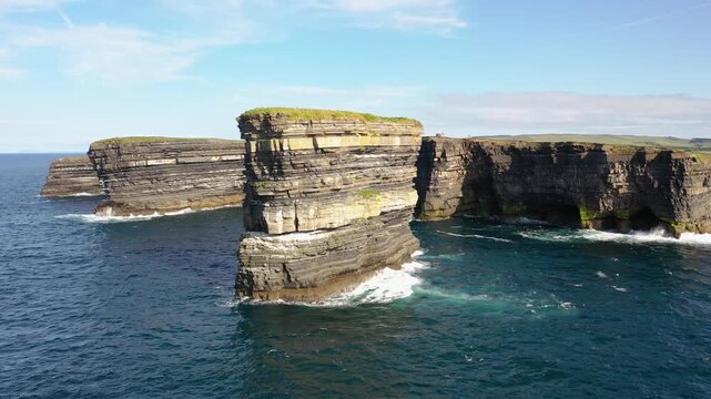 Aerial view of Dun Briste sea stack rising from the Atlantic Ocean with layered rock cliffs and blue water in Ballycastle, County Mayo, Ireland.
