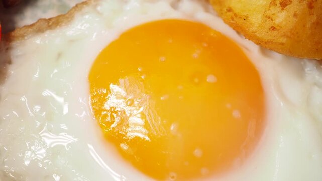 Close up motion of a delicious fried egg with golden yolk and crispy potato wedge.
