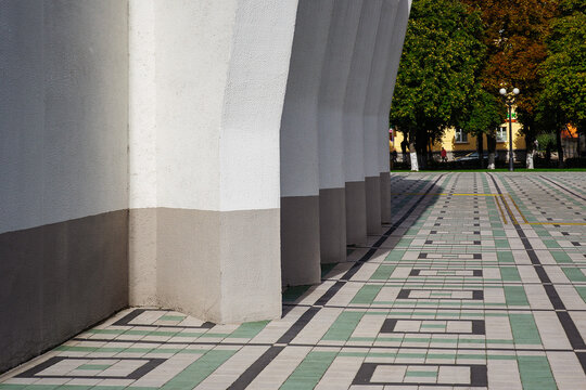 Geometric concrete columns of modern building facade casting shadows on patterned tiled pavement on sunny day with copy space