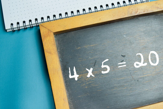 Chalkboard with phrase 4 x 5 = 20 multiplication equation on wooden desk. For basic arithmetic and school education