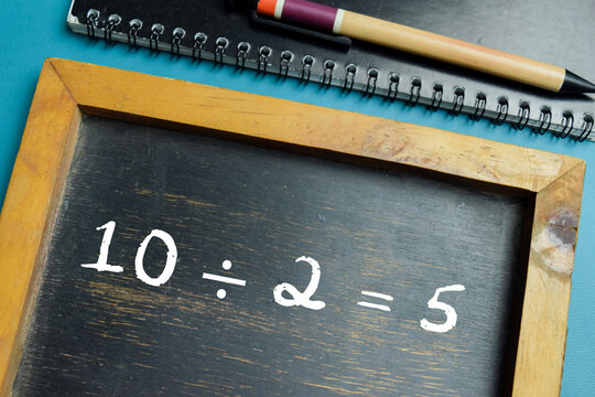 Chalkboard with phrase 10 &divide; 2 = 5 math equation on wooden desk. For basic division and primary school education