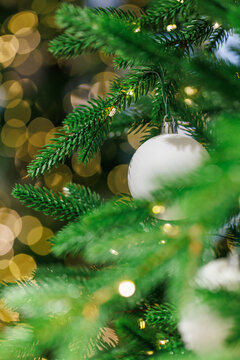 White Christmas ornament on fir tree with golden bokeh lights