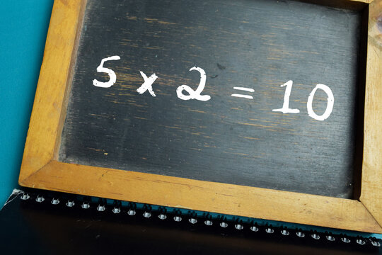Chalkboard with phrase simple 5x2=10 math equation on wooden desk. For basic multiplication and primary school education