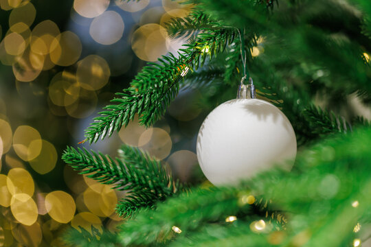 White Christmas ornament on fir tree with golden bokeh lights