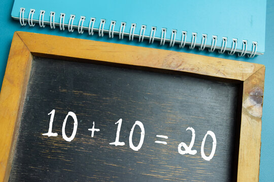 Chalkboard with phrase simple 10+10=20 math equation on wooden desk. For basic addition and primary school education