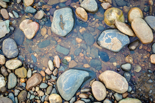 Colorful river stones and pebbles underwater with clear water stream texture