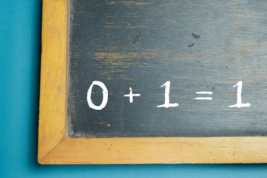 Chalkboard with phrase 0 + 1 = 1 addition equation on wooden desk. For school education and learning