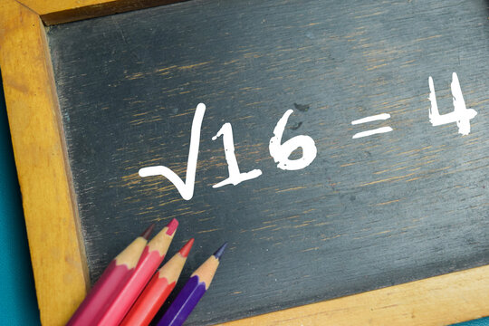 Chalkboard with phrase &radic;16 = 4 square root equation on wooden desk. For basic mathematic arithmetic