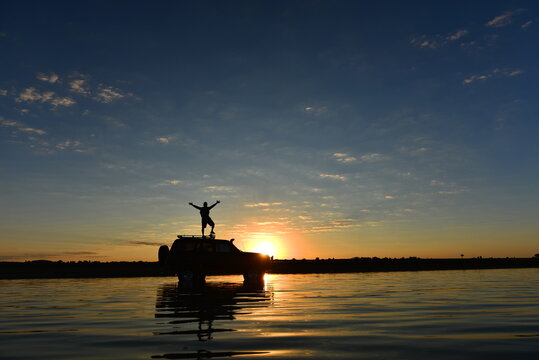 Epic off-road adventure journey with a 4x4 vehicle parked in water and a traveler enjoying the scenic sunrise view.