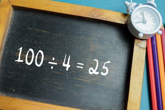 Chalkboard with phrase 100 &divide; 4 = 25 division equation on wooden desk. For basic arithmetic and school education