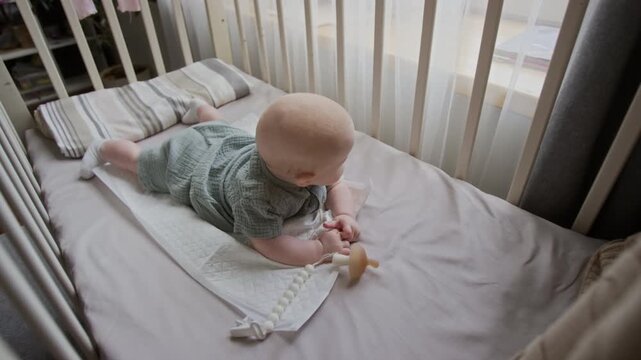 Portrait of Caucasian baby practicing tummy time inside crib. Clip serves parenting advertisements, pediatric healthcare promotions, or infant product campaigns