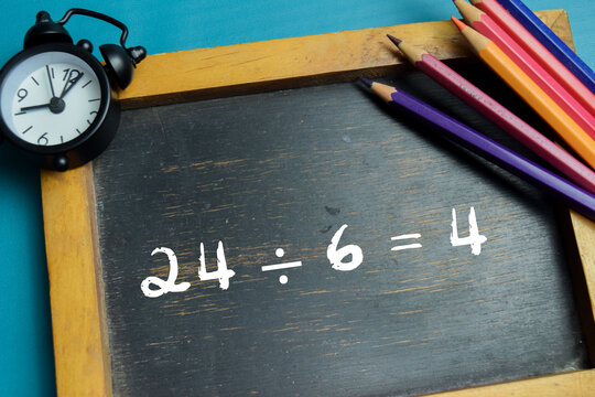 Chalkboard with phrase 24 &divide; 6 = 4 division equation on wooden desk. For basic arithmetic and school education
