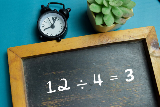 Chalkboard with phrase 12 &divide; 4 = 3 division equation on wooden desk. For basic arithmetic and school education