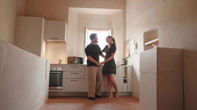 Young man and woman in love standing in their minimalist kitchen, holding hands and talking sweetly to each other, sharing a quiet, affectionate moment together at home