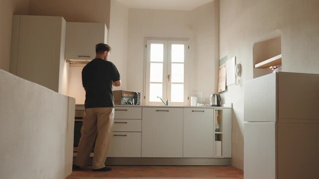 Millennial man preparing breakfast and making fresh coffee in his modern bright kitchen, enjoying a cozy and tranquil morning routine while starting his day with energy