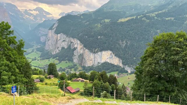 Lauterbrunnen Valley opens below green hills and towering rock cliffs, Traditional Swiss barns and villages appear across the scenic Alpine landscape