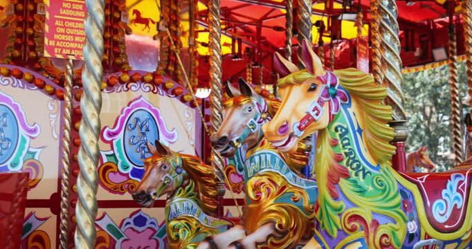 Panning close-up view of ornately painted carousel horses with gold and red scrollwork on a traditional fairground ride.