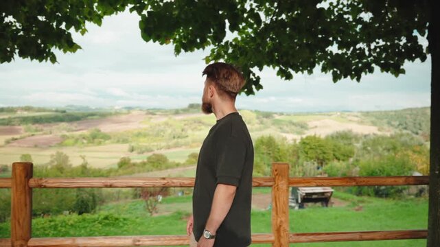 Young bearded man enjoying the stunning view of the rolling hills and green landscape of tuscany, italy during a peaceful and relaxing summer vacation in the countryside