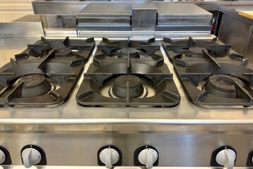 Front view of professional industrial gas stove with multiple burners and white control knobs in restaurant kitchen. Modern commercial catering equipment supports efficient cooking in hospitality venu © Ana