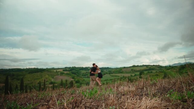 Romantic young couple running towards each other for a loving embrace and kiss on a hill with a beautiful view of the tuscan countryside, feeling happy and free