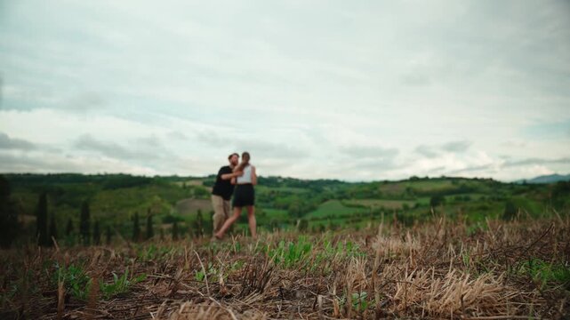 Romantic young couple joyfully running and hugging in a beautiful tuscan field, expressing freedom and love with a scenic green hill landscape in the background