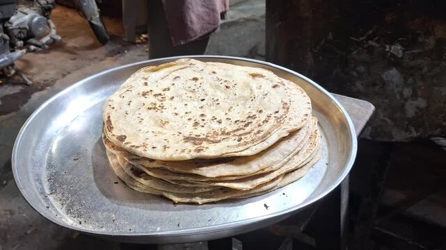 Stack of freshly cooked hot traditional Indian chapatis or roti flatbreads served on a metal plate in a rustic kitchen setting, close up video
