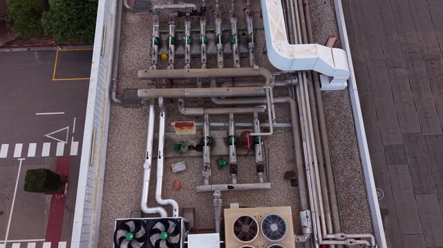 Overhead view of industrial rooftop HVAC system with metal pipes, valves, pump manifolds and white ductwork on a commercial building rooftop