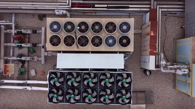 Top-down view of industrial rooftop HVAC units with multiple cooling fans, pipes and mechanical equipment on a gravel rooftop surface