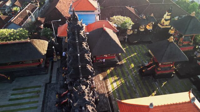 Balinese temple courtyard with thatched roof pavilions near local houses in morning light showcasing historic Asian architecture overhead aerial drone footage