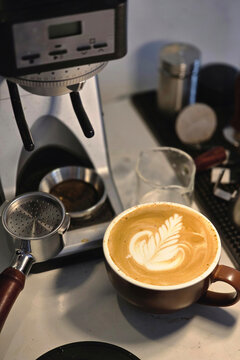 Freshly Prepared Latte with Rosetta Latte Art Beside Coffee Grinder and Portafilter.