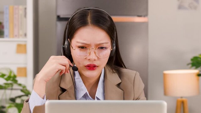 Frustrated Asian Businesswoman Wearing Headset Having Online Video Conference at Home