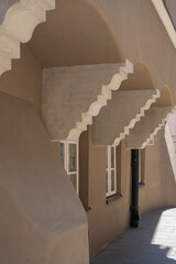 Decorative stone corbels support the curved stucco facade of a historic European building. Small windows and a downspout line the beige wall along a sunny paved street in Warsaw old town. © dimetradim