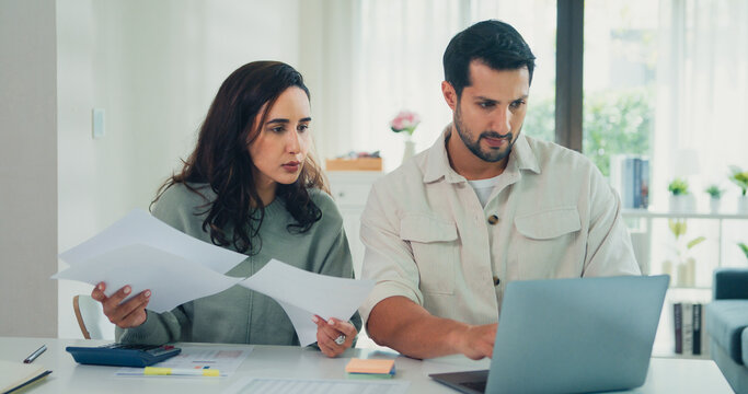 Young Latin couple male, female serious focus on laptop computer check document paper pay bills online plan budget expense in living room at home. Marriage money trouble, Family budget plan concept.