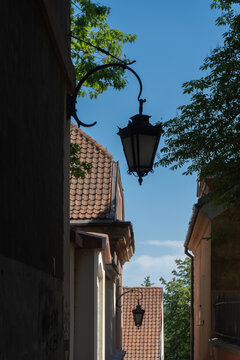 Antique wrought iron lantern hangs on a historic building facade. Narrow alley with tile roofs and traditional street lamps in old European town. Cozy urban district exterior design.