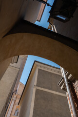Low angle view of ancient stone arch and residential building facades in Warsaw. Traditional architectural elements form a narrow medieval alley for historic travel and design blog. © dimetradim