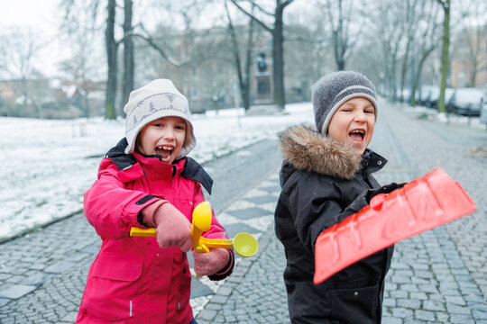 Portrait two cute little kids boy girl enjoy having fun playing with snow toys city street park  family on snowy cold winter day. Children carefree joy walk outdoors. Happy childhood healthcare