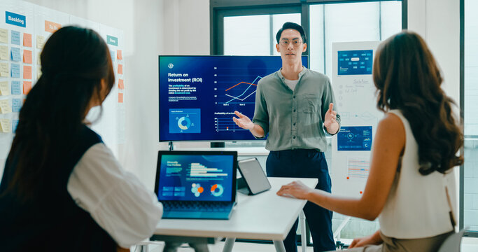 Group of Asian businesspeople work together leads business meeting uses presentation TV with revenue, profit or sale statistics in office. Financial generation z team brainstorm on e-Commerce project.