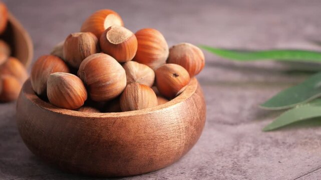 Close up video of hazelnuts in a wooden bowl with blurry background shot in motion, capturing organic and wholesome snack.