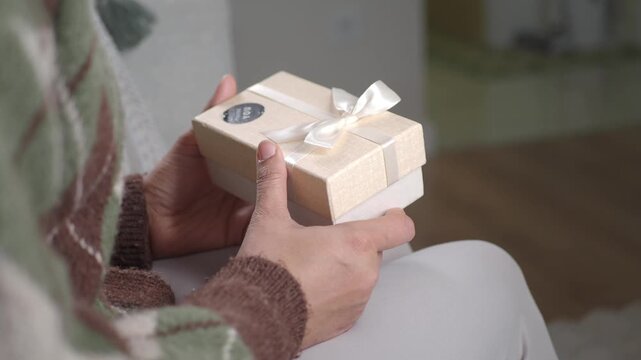 Close up on hands holding gift box tied with ribbon, receiving present, thoughtful moment.
