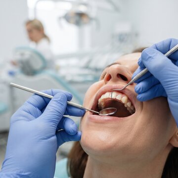 Close up view of young woman relaxes and open mouth while a dentist inspects her teeth using a mirror and probe during a routine dental exam.
