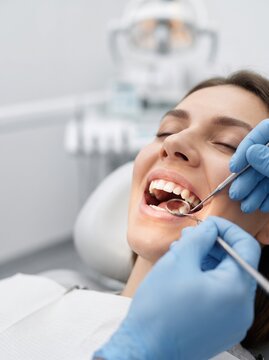 Close up view of young woman relaxes and open mouth while a dentist inspects her teeth using a mirror and probe during a routine dental exam.