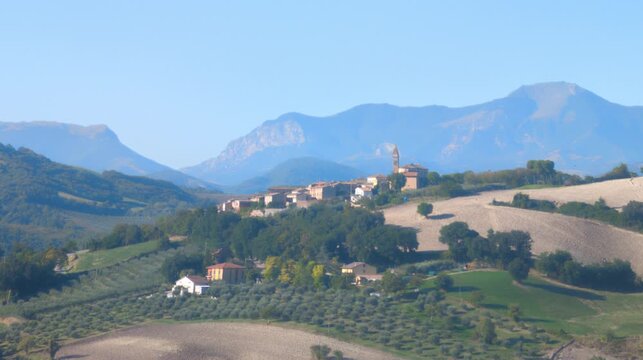 Panoramica di un caratteristico borgo italiano adagiato sulle colline, con maestose montagne sullo sfondo