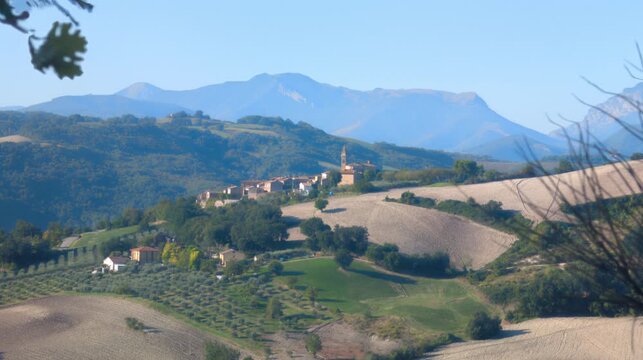 Panoramica di un caratteristico borgo italiano adagiato sulle colline, con maestose montagne sullo sfondo