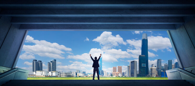 Businessman raising arms celebrating success looking at city skyline